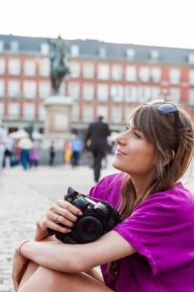 Jovem turista segurando uma câmera fotográfica, sentado e olhando para edifícios na Praça Plaza Mayor, Madrid, Espanha — Fotografia de Stock