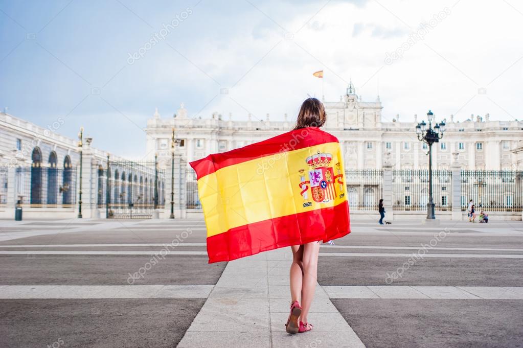 Young woman in front of Palacio de Oriente - the Royal Palace of Madrid, holding a flag.