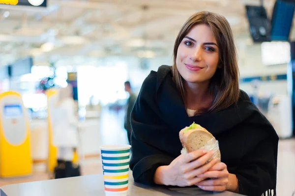 Mujer joven en el aeropuerto internacional, bebiendo café y comiendo un sándwich —  Fotos de Stock