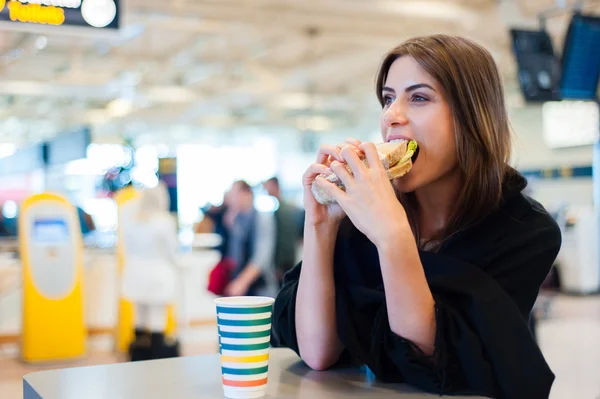 Junge Frau am internationalen Flughafen, trinkt Kaffee und isst ein Sandwich — Stockfoto