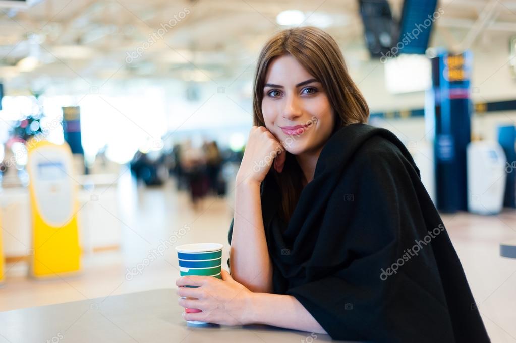 Young woman at international airport, drinking coffee while waiting for her flight.