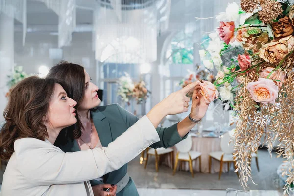 Beautiful women, girls florists in stylish suits in restaurant looking at floral composition. Wedding organizers, event decorators. Business meeting,negotiations,signing contract with client,customer.