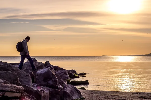 Traveller walking on rock cliff against sea, sunrise or sunset — Stock Photo, Image