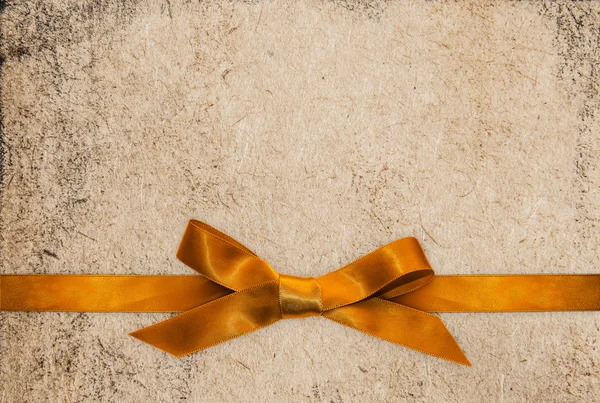 Gold ribbon bow on paper textured background — Stock Photo, Image
