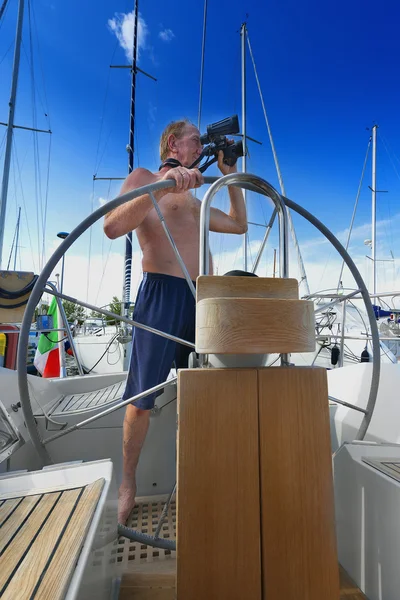 man at the helm of sailboat looking through binoculars