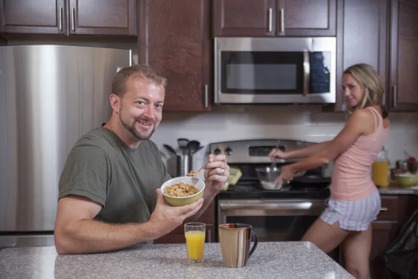 Homem come cereais enquanto senhora faz café da manhã — Fotografia de Stock