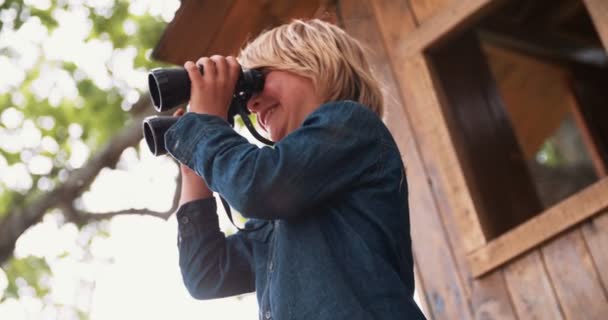 Ragazzo seduto in una casa sull'albero guardando attraverso il binocolo — Video Stock