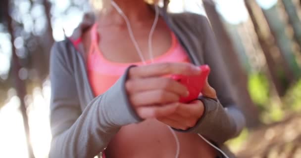 Läufer im Kapuzenpulli mit Handy mit Kopfhörer auf Naturlehrpfad — Stockvideo