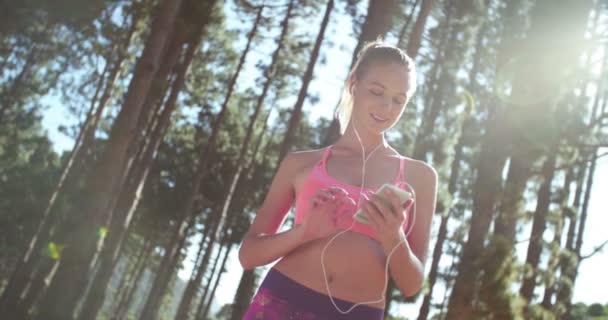 Kvinnan jogger i en skog med telefon och hörlurar — Stockvideo