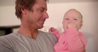 Dad Holding and Smiling at Infant Daughter Indoors