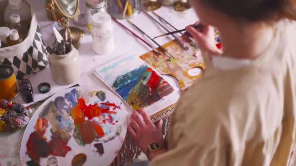 Художник рисует на бумаге с палитрой и яркими красками — стоковое видео