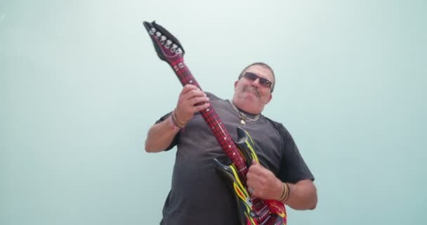 Смешной человек, играющий на надувной гитаре — стоковое видео