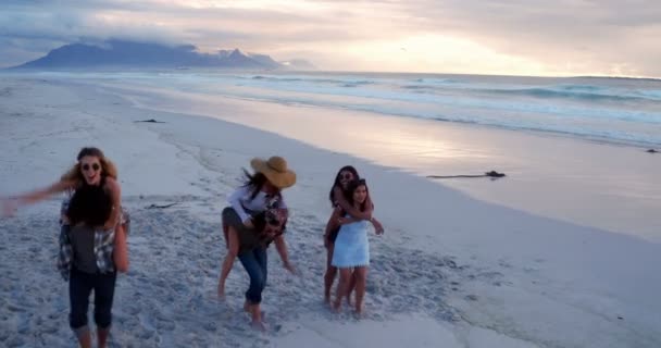 Freunde mit lustigen Huckepackfahrten am Strand — Stockvideo