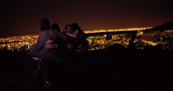 Teens hugging on a convertible looking at night city — Stockvideo