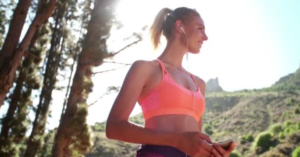Woman runner wearing earphones selecting music on her phone — Stock Video