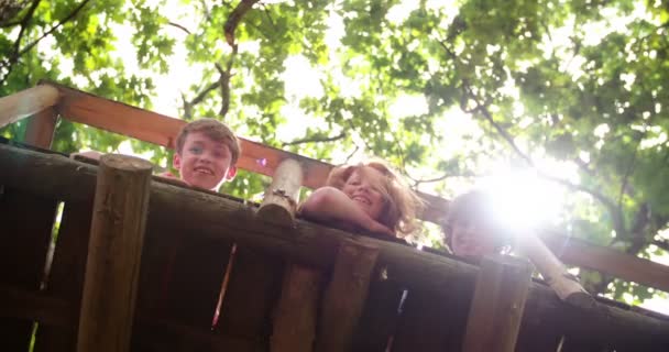 Kinderen kijken over kant van treehouse met bladeren — Stockvideo