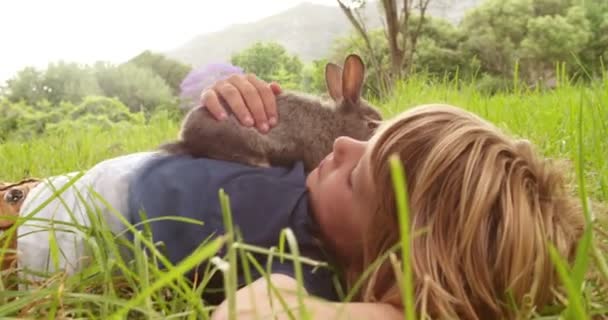 Junge genießt sein Häschen, das draußen auf Gras liegt — Stockvideo