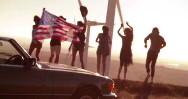 Amigos camino tropezando a parque eólico llevando bandera americana — Vídeo de stock