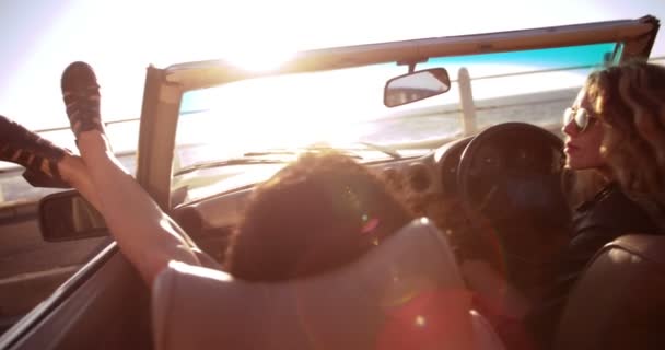 Amigos disfrutando de la puesta de sol sentado en un convertible vintage — Vídeo de stock