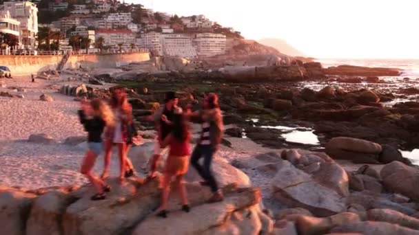 Barátok táncolnak a strandon naplementekor — Stock videók
