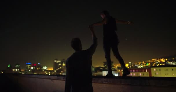 Чоловік тримає руку з дівчиною, яка балансує на краю даху — стокове відео