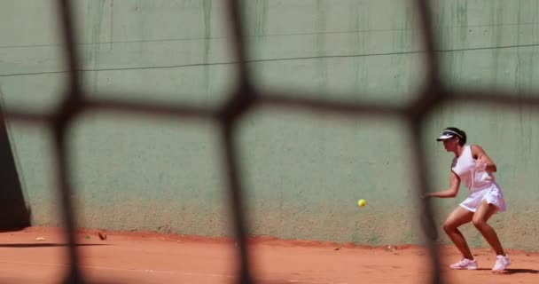 Женщина играет в теннис пова через кортовую сеть — стоковое видео