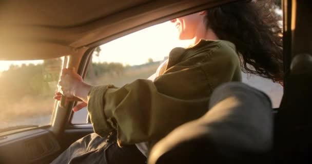 Mladá žena se při západu slunce naklání z okna auta — Stock video