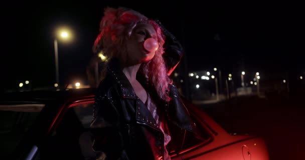 Ροζ μαλλιά νεαρή γυναίκα ακουμπά στο αυτοκίνητο μασώντας τσίχλα — Αρχείο Βίντεο
