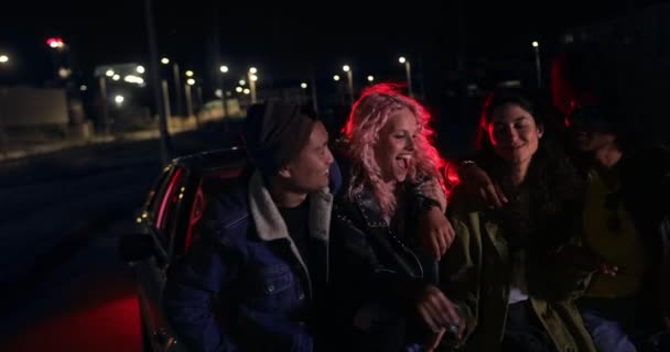 Группа друзей развлекается, опираясь на машину ночью — стоковое видео