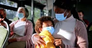 Afro-Amerikalı bir kadın otobüste uyuyan bir çocuğu tutuyor.