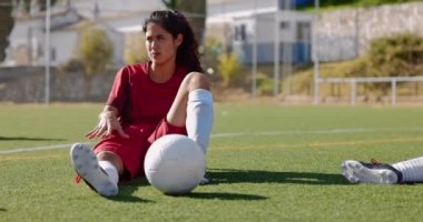 Futbol oyuncusu antrenmandan sonra takım arkadaşlarıyla çim sahada dinleniyor.