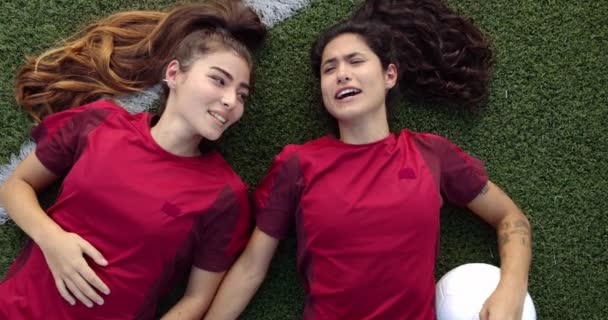 Dos felices compañeras de equipo de fútbol relajándose tumbadas en la hierba — Vídeos de Stock