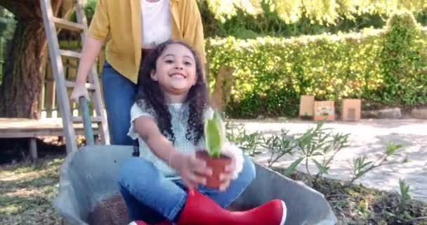 Mamá jugando con una niña en carretilla en un jardín — Vídeos de Stock