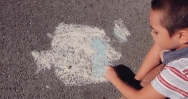 Küçük çocuk asfalt yolda tebeşirle çiziyor.