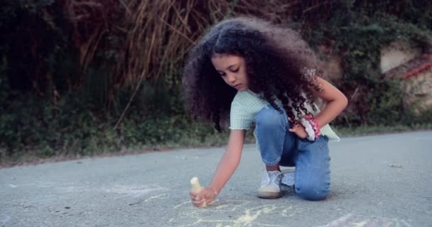Nettes kleines Mädchen zeichnet mit Kreide auf Asphaltstraße — Stockvideo