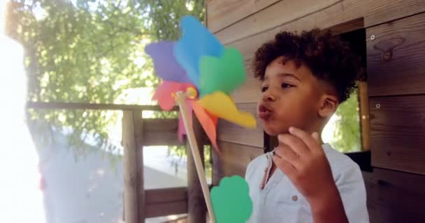 Kleine jongen blaast kleurrijke pinwheel op de top van boomhut — Stockvideo