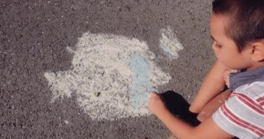 Küçük çocuk asfalt yolda tebeşirle çiziyor.