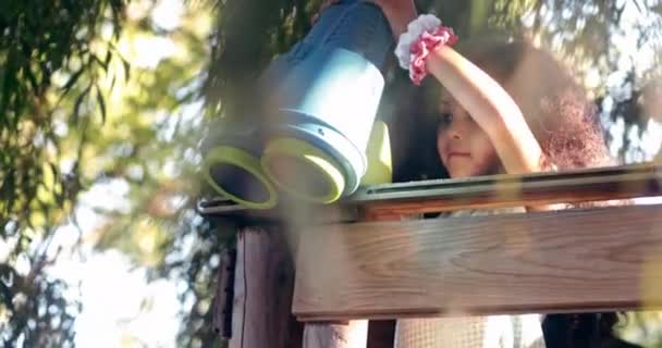 Девочка смотрит в бинокль на домике на дереве на детской площадке — стоковое видео
