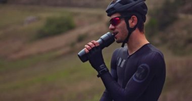 Profesyonel bisikletçi seyahat şişesinden su içiyor.