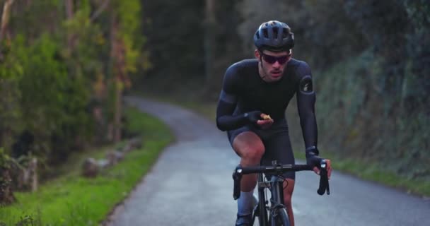 Professional cyclist riding bicycle and eating snack bar outdoors — Stock Video