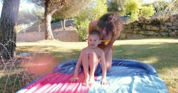 Мати штовхає сина на садовий водяний слайд — стокове відео