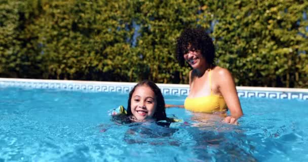Madre ayudando a su hija a nadar con flotadores en una piscina — Vídeos de Stock
