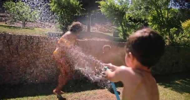 Madre e hijos siendo salpicados con manguera de agua por niño — Vídeos de Stock