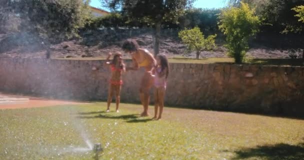 Moeder en meisjes spelen in de zomer met tuinsproeier — Stockvideo