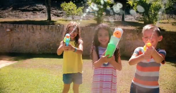 Група дітей, які прицілюють водяний пістолет до камери на городі — стокове відео