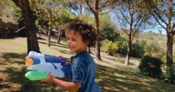 Chłopiec działa i bawi się pistoletem wodnym w ogrodzie — Wideo stockowe