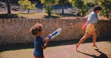 Anne ve çocuk bahçede su tabancasıyla oynuyorlar.