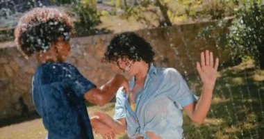 Anne ve çocuk su sıçratıyor ve bahçe fıskiyesiyle oynuyor.