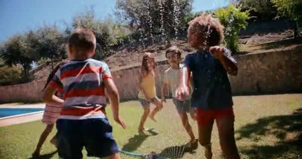 Grupo de niños jugando y saltando sobre aspersores en el jardín — Vídeos de Stock