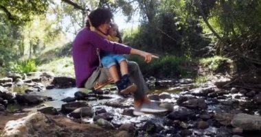 Anne ve kızı salıncakta sallanıyor ve nehre bakıyor.